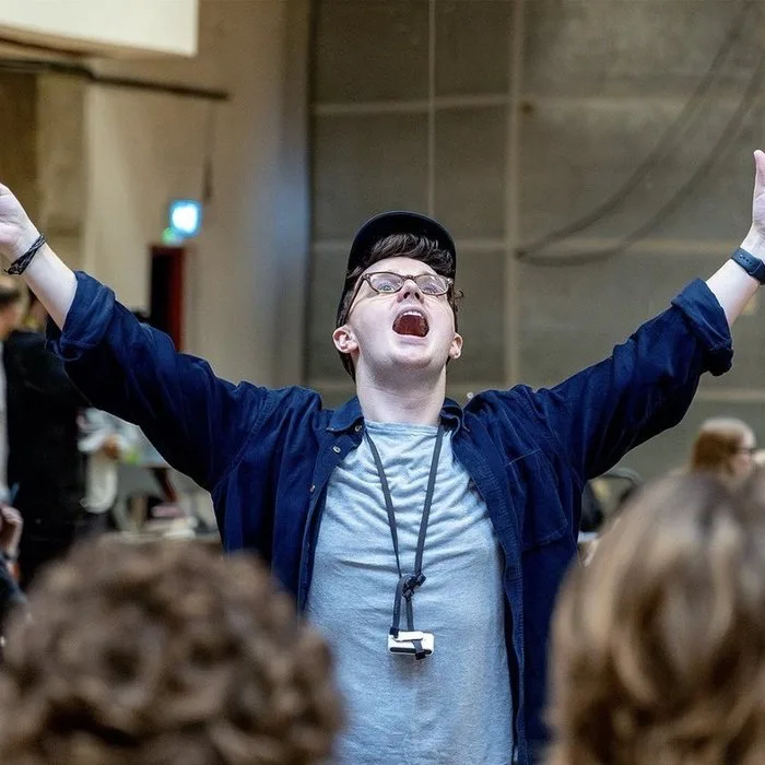 Luke Holman in a rehearsal room, arms flung wide, pencil in hand